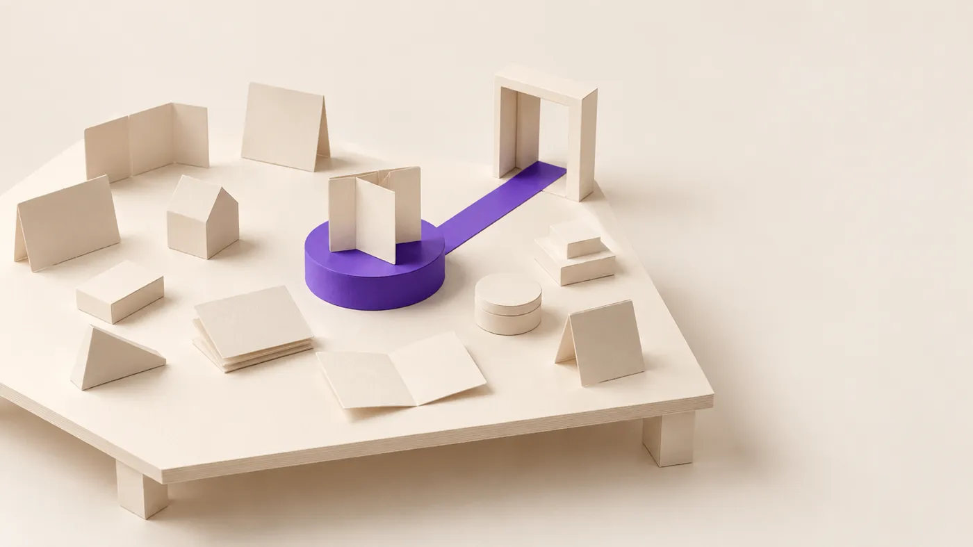 maquete de papel: muitos protótipos pequenos espalhados numa mesa; um deles, sobre um pedestal violeta, ligado por um trilho a uma porta.